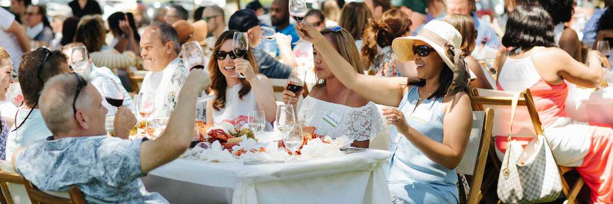 people sitting at tables at an outdoor party raising their wine glasses