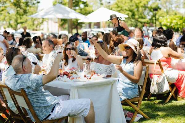 people sitting at tables at an outdoor party raising their wine glasses