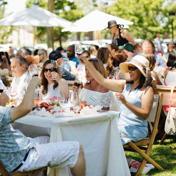 people sitting at tables at an outdoor party raising their wine glasses