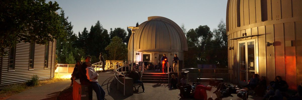 People stargazing by observatory domes under a bright moonlit sky.