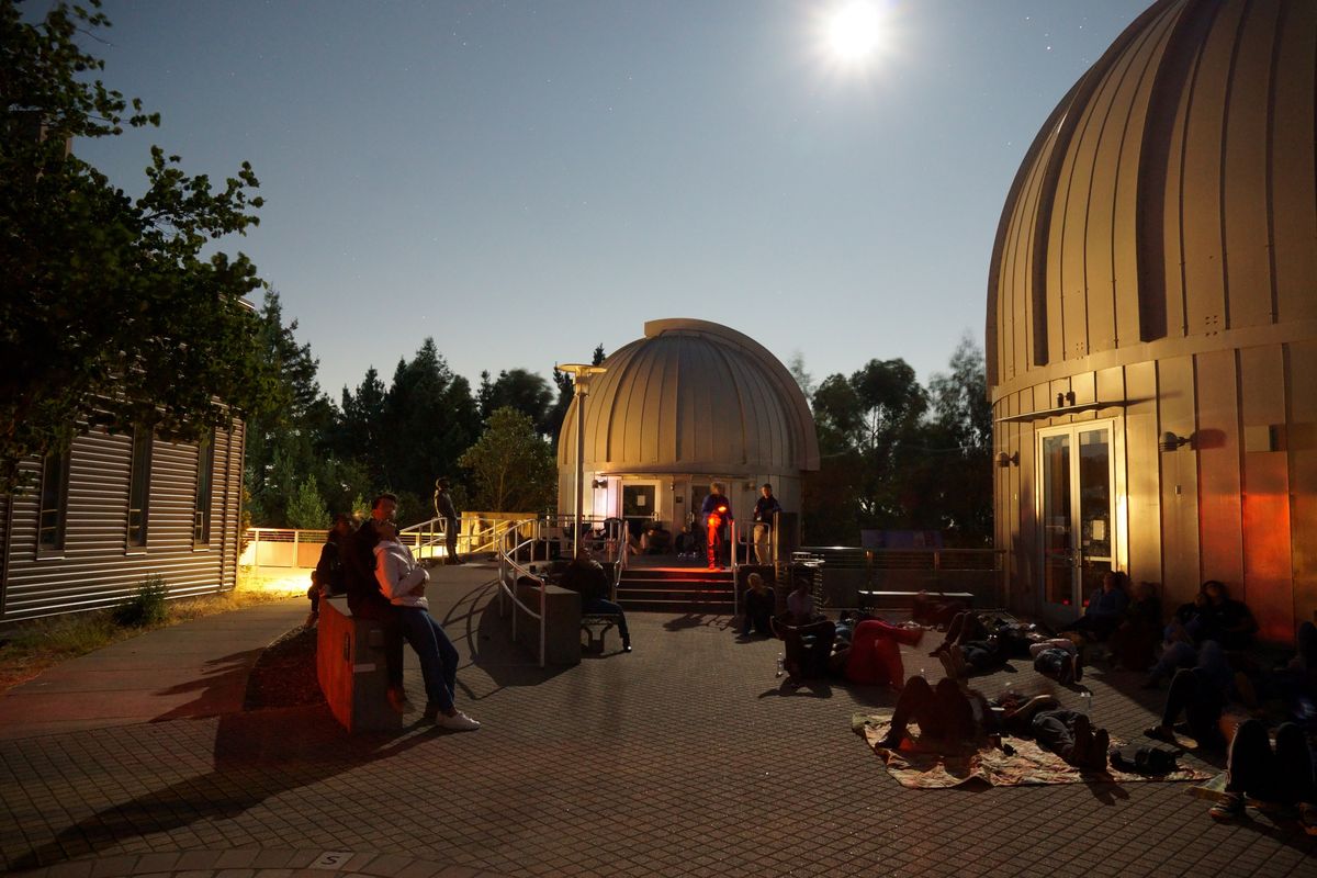 People stargazing by observatory domes under a bright moonlit sky.