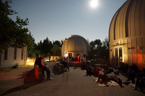 People stargazing by observatory domes under a bright moonlit sky.