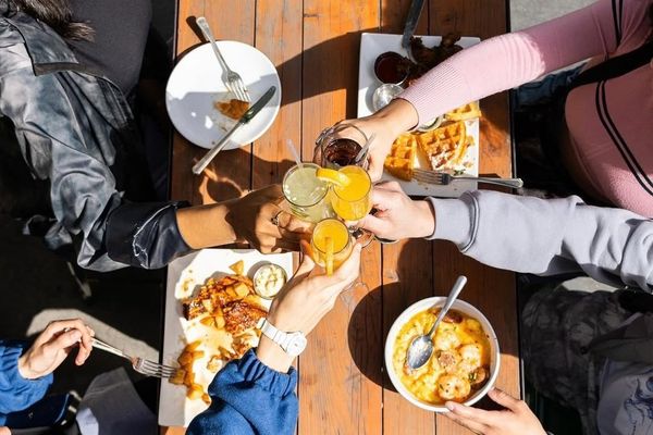People toasting with drinks over a table of brunch food.