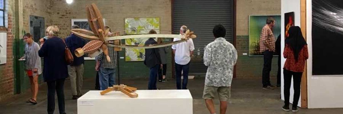 People viewing artworks in an industrial-style gallery with modern sculptures and paintings.