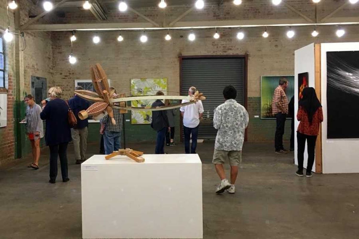 People viewing artworks in an industrial-style gallery with modern sculptures and paintings.