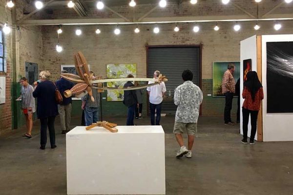 People viewing artworks in an industrial-style gallery with modern sculptures and paintings.