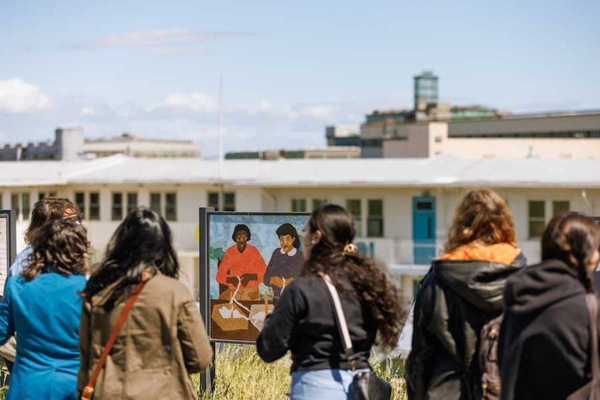 People viewing outdoor art exhibit with paintings in front of a building.