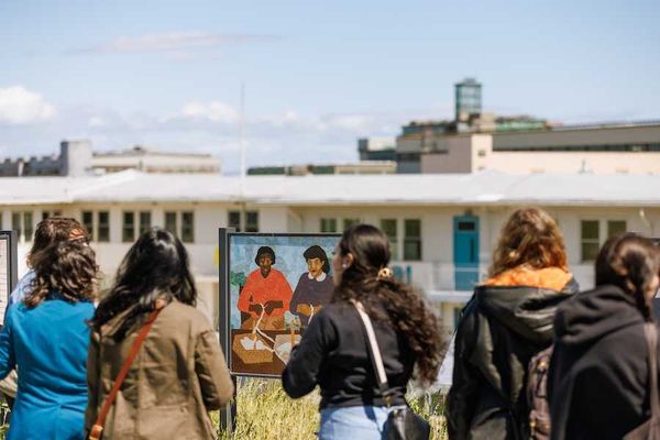People viewing outdoor art exhibit with paintings in front of a building.