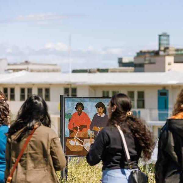 People viewing outdoor art exhibit with paintings in front of a building.