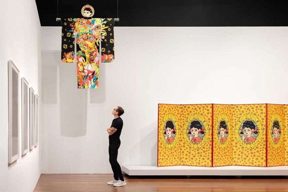 Person admiring vibrant kimono art and yellow screen in a gallery.