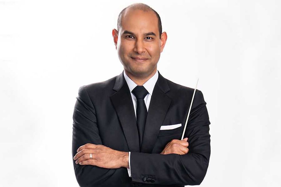 Person in a suit holding a conductor's baton against a white background.