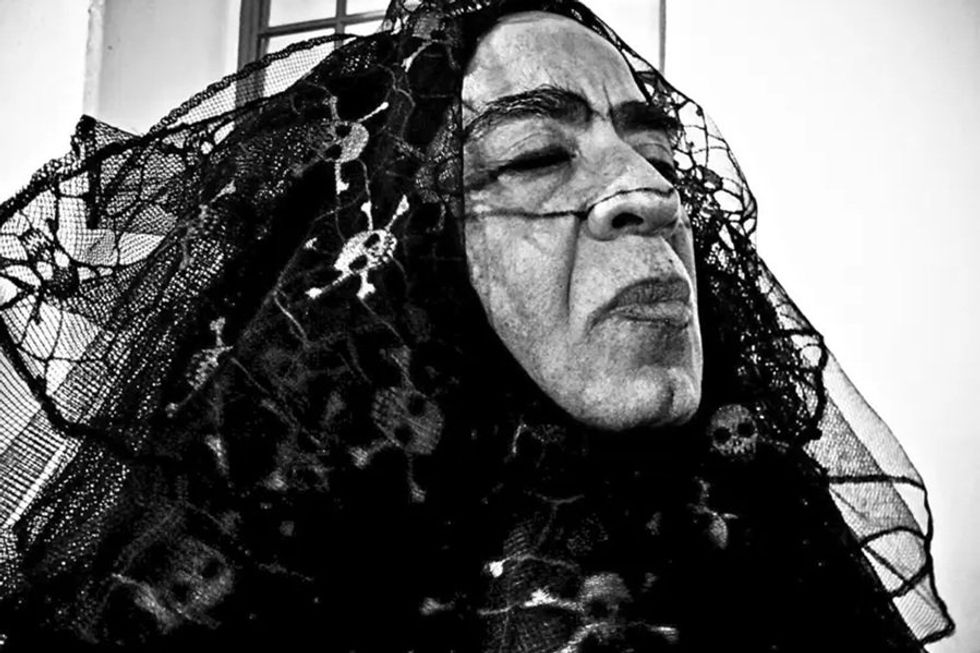 Person in lace veil with skull pattern, eyes closed, in a black and white photo.