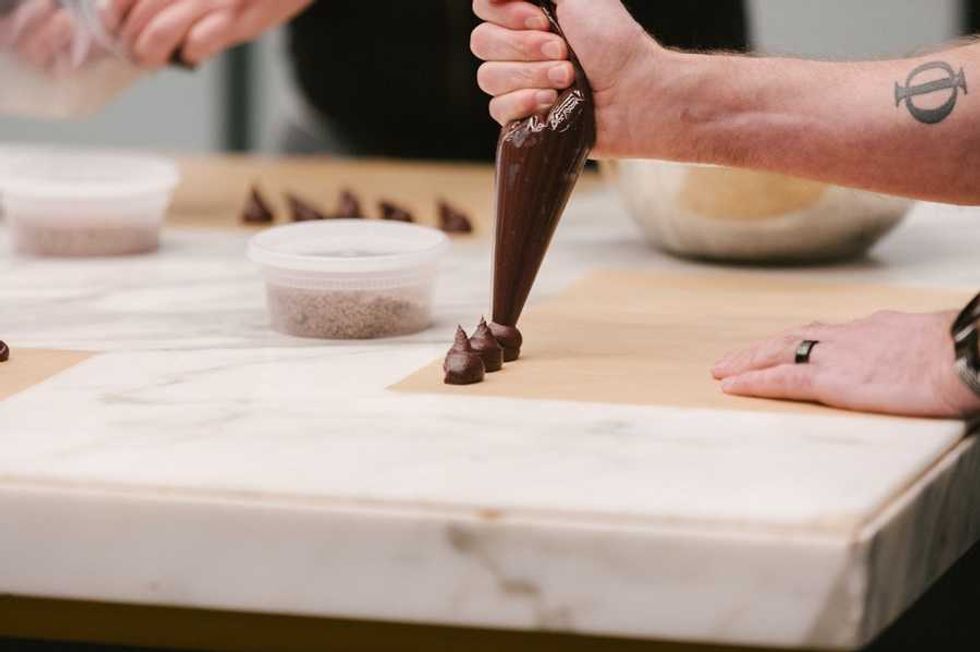Person piping chocolate dollops onto parchment paper.