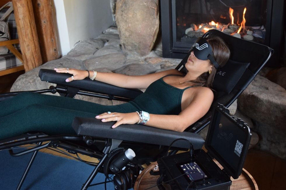Person relaxing in a recliner with a mask, near a fireplace, using wellness technology.