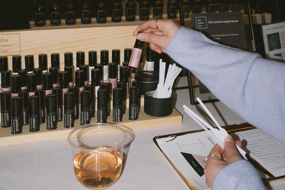 Person sampling perfumes at a scent bar with test strips and a drink.