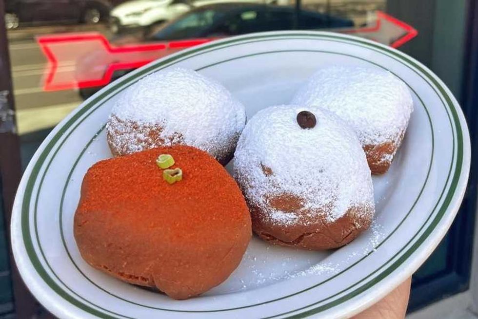 Plate with powdered and cinnamon-sprinkled donuts, one topped with chocolate, outdoors.