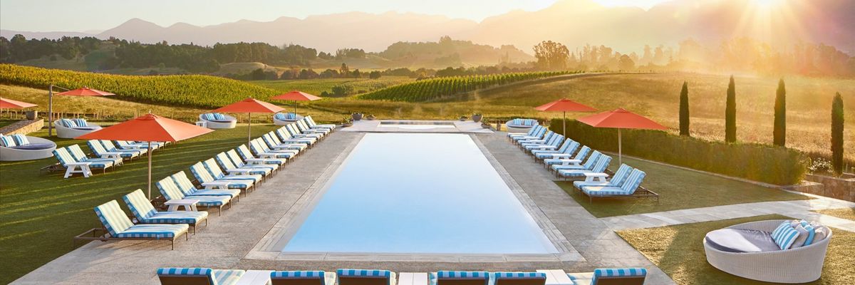Pool with lounge chairs, umbrellas, and mountain sunset in the background.