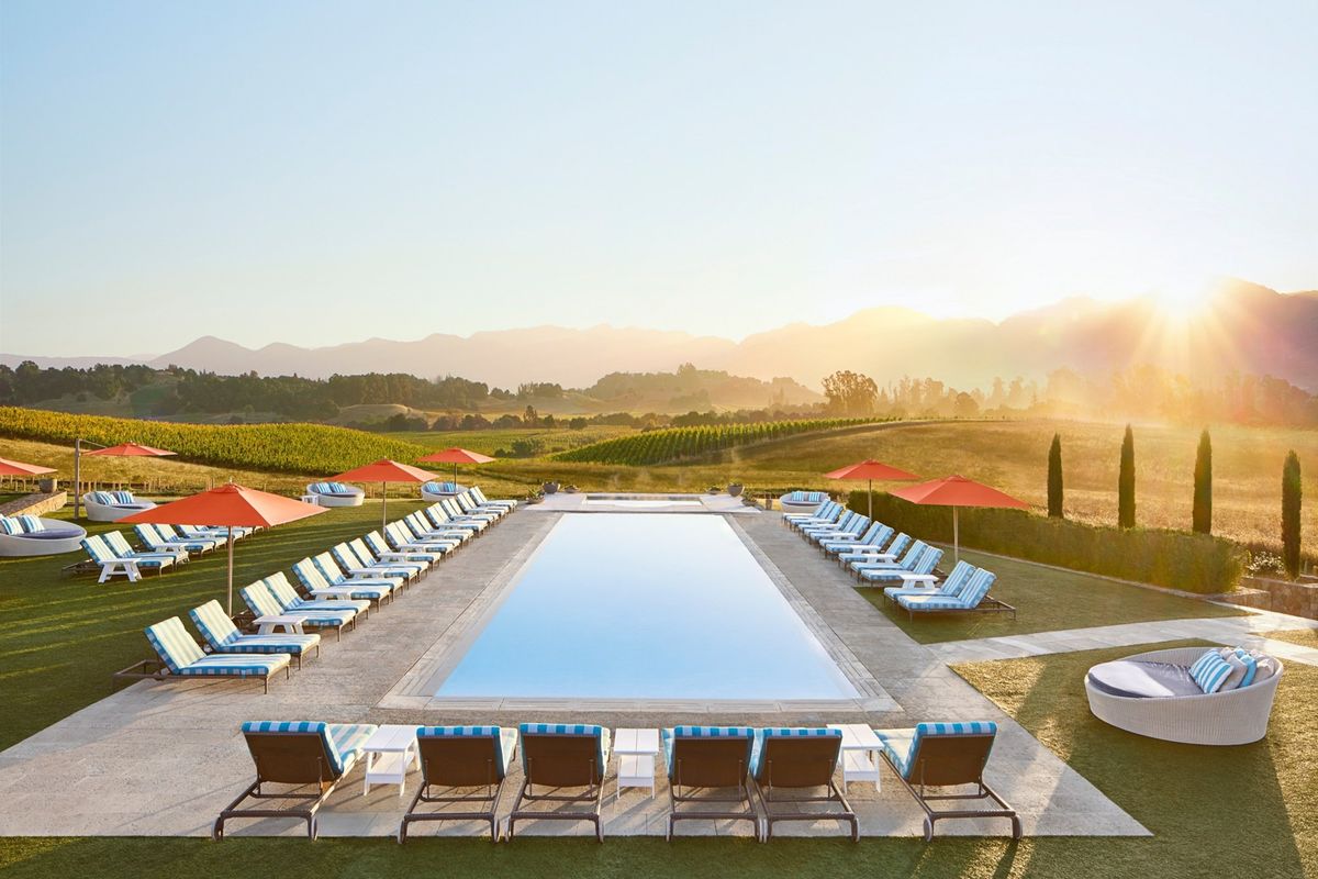Pool with lounge chairs, umbrellas, and mountain sunset in the background.
