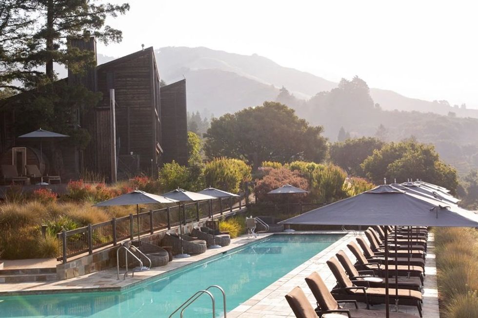 Poolside chairs and umbrellas beside lush greenery and mountains in the background.