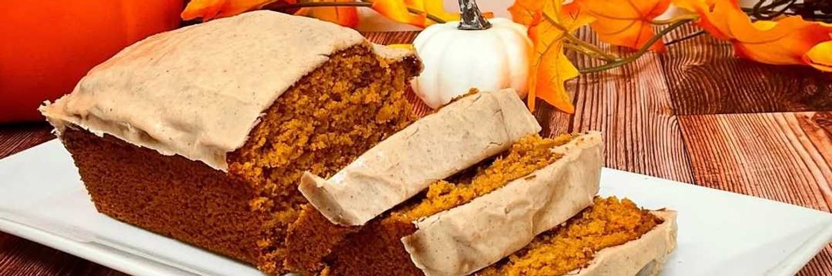Pumpkin bread with frosting, surrounded by pumpkins and autumn leaves on a wooden table.