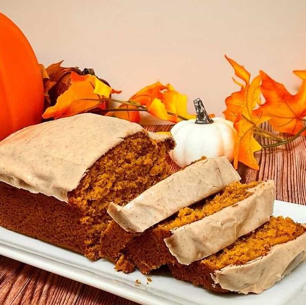 Pumpkin bread with frosting, surrounded by pumpkins and autumn leaves on a wooden table.