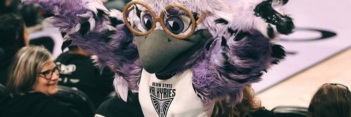 Purple-feathered bird mascot with glasses, cheering at a sports event.