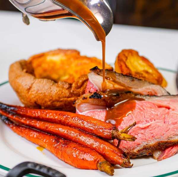roast meat with Yorkshire pudding and roast carrots being drizzled with jus