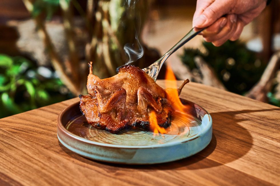 Roasted quail on fire, served on a ceramic plate, with a fork in hand above.