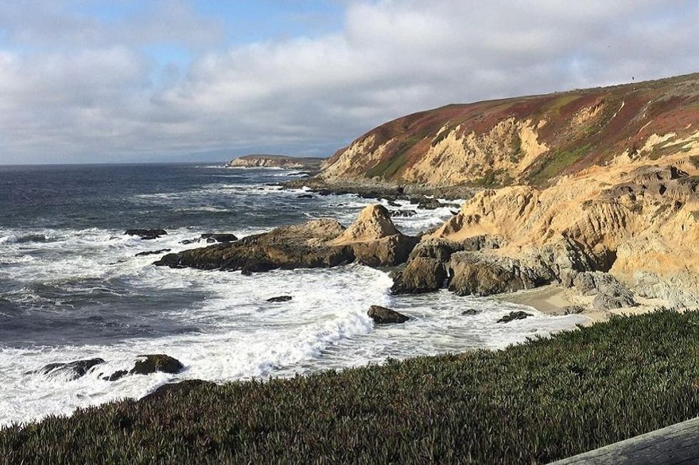 Rocky coastline with waves crashing, under a partly cloudy sky.