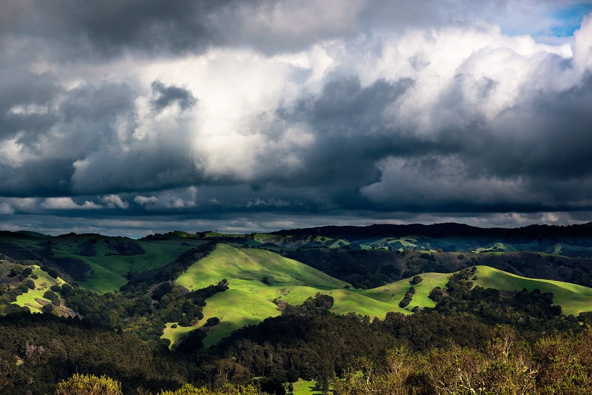 Rolling green hills under dramatic, cloudy sky.