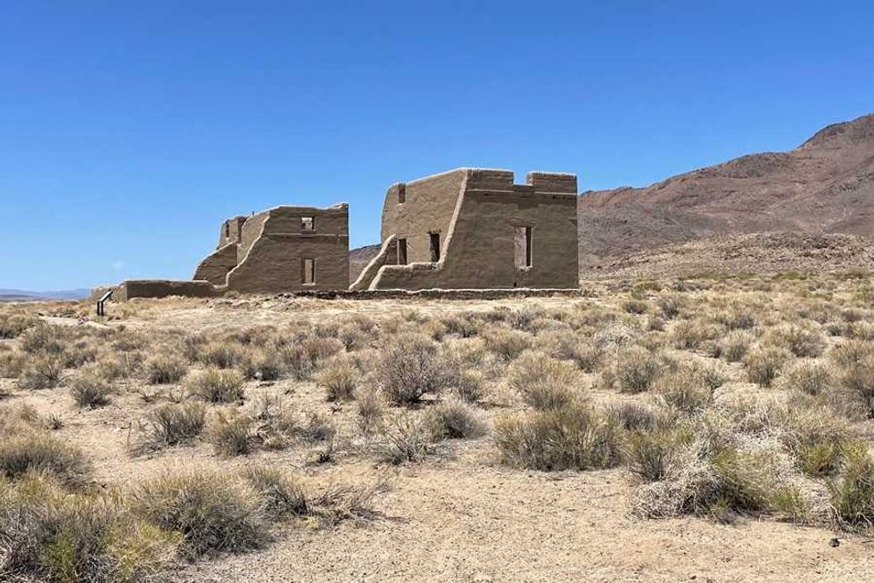 Ruins of adobe buildings in a desert landscape with a clear blue sky.
