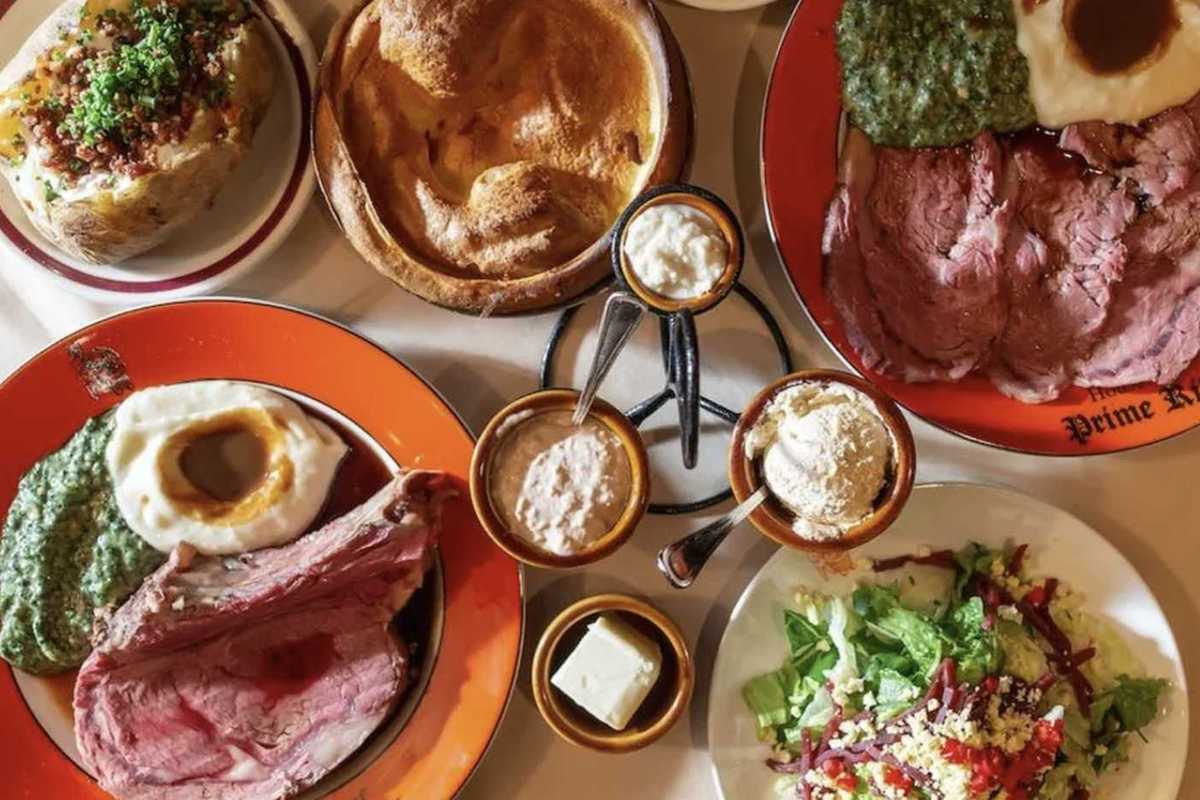 several dishes of steak and other steakhouse foods on a table and orange plates that say 'House of Prime Rib'