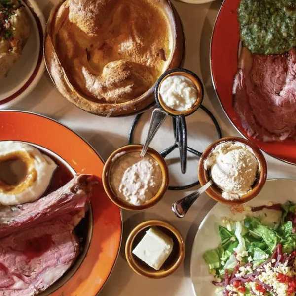 several dishes of steak and other steakhouse foods on a table and orange plates that say 'House of Prime Rib'