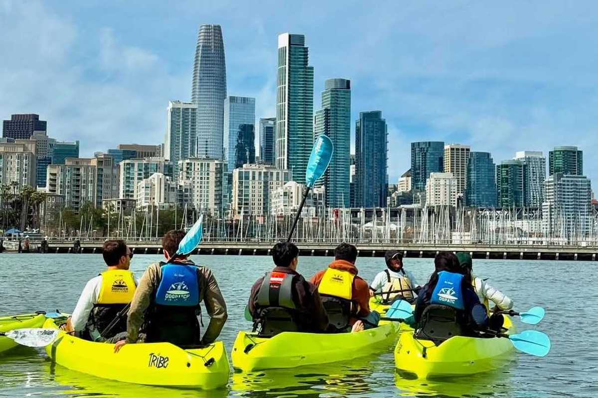 Several yellow kayaks in the water with downtown San Francisco in the background