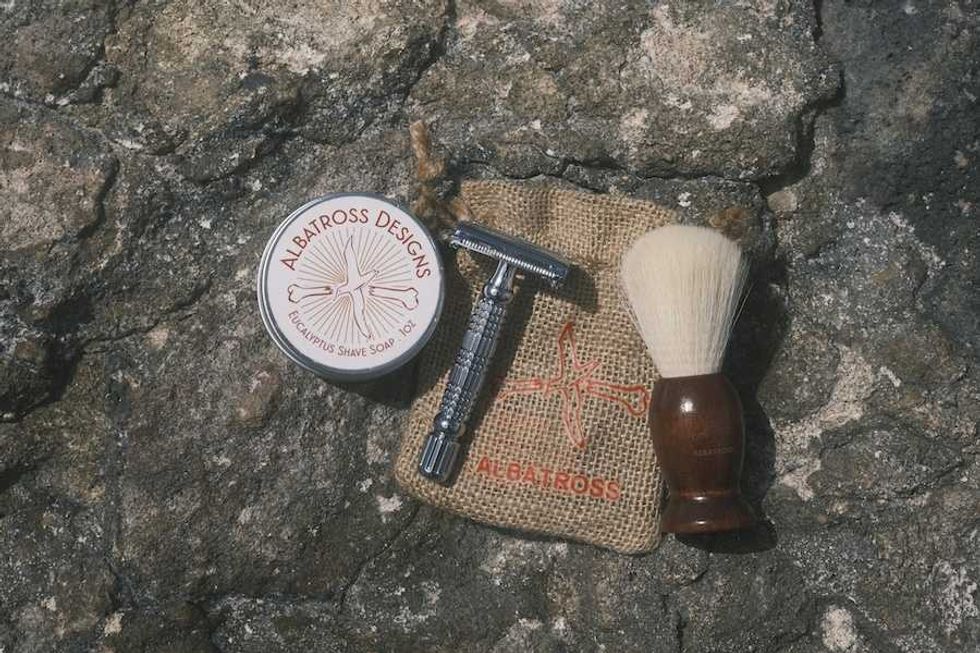 Shaving kit with razor, brush, and shave soap on a textured rock surface.