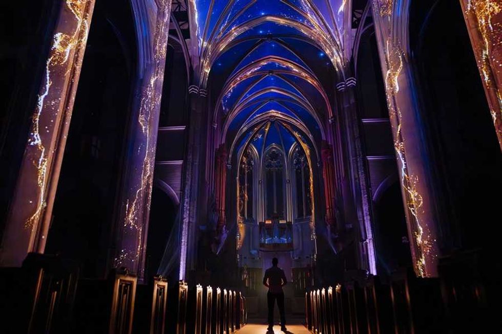 Silhouetted person in a cathedral with illuminated, colorful arches and columns.