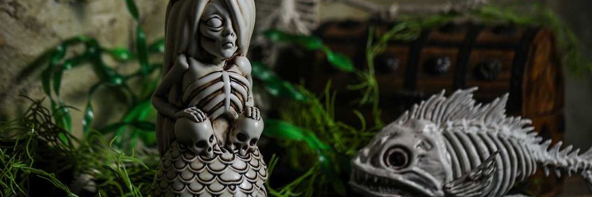 Skeleton mermaid mug with skulls and plants, fish and treasure chest in background.