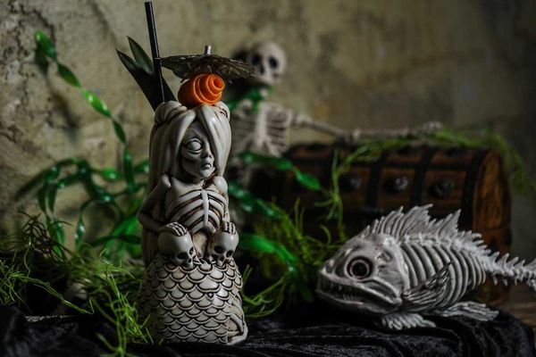 Skeleton mermaid mug with skulls and plants, fish and treasure chest in background.