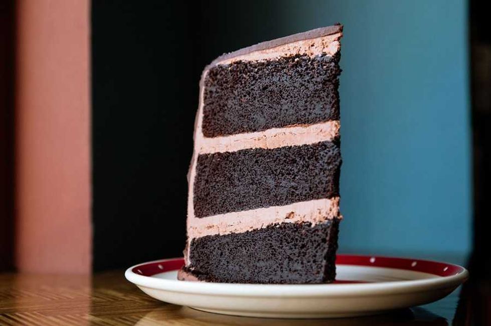 Slice of chocolate cake with layers of frosting on a plate.