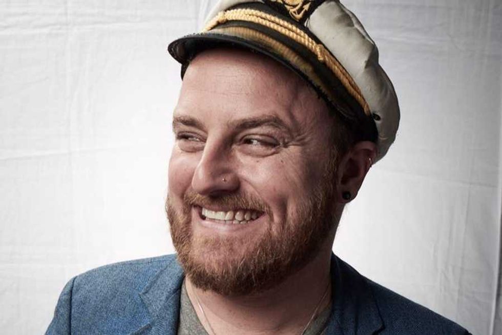 Smiling man in a captain's hat with a beard and blue blazer.
