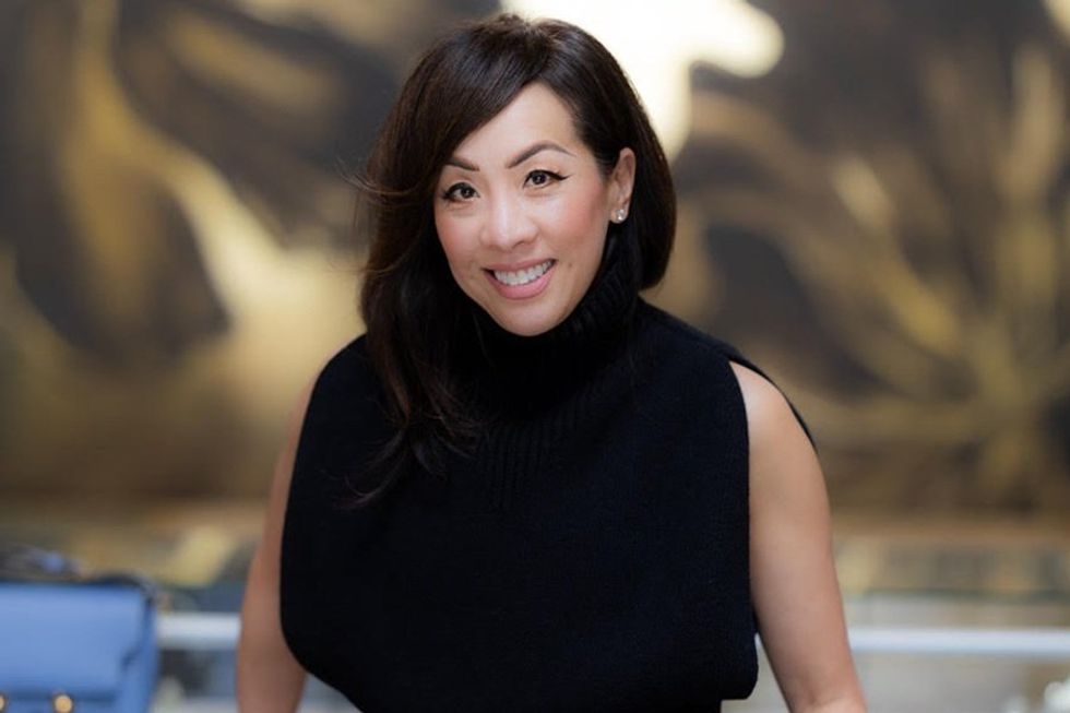 Smiling woman in a black sleeveless turtleneck top, blurred background.