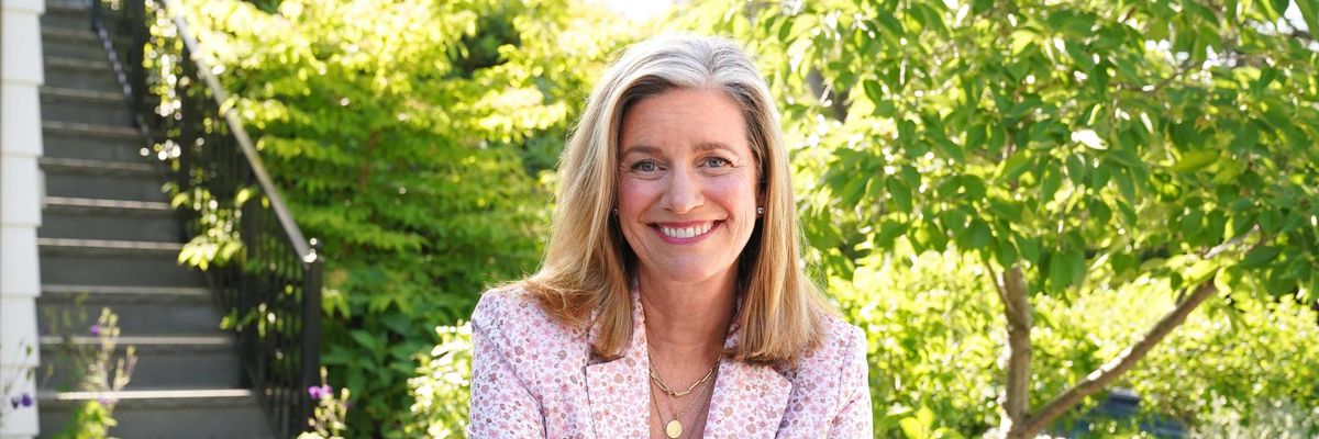 Smiling woman in a garden sitting at a table, wearing a floral-patterned blazer.