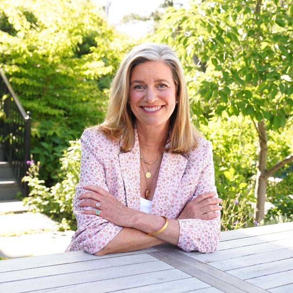Smiling woman in a garden sitting at a table, wearing a floral-patterned blazer.