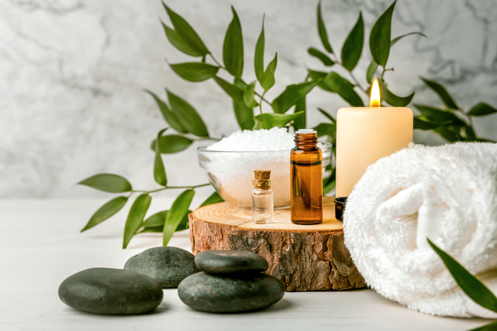 Spa essentials with candle, oils, towel, and stones on wooden surface.