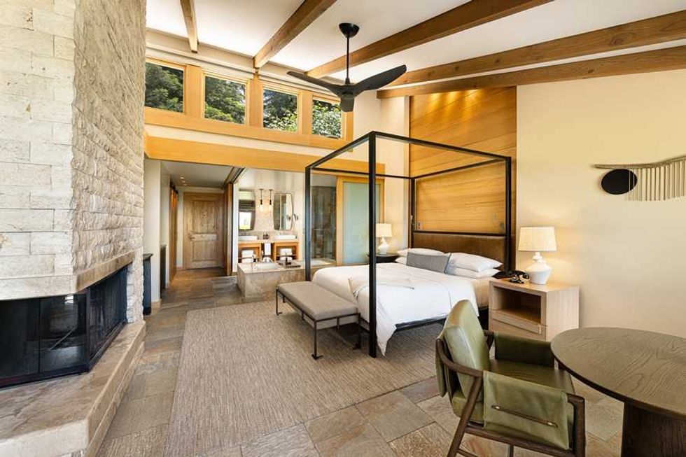 Spacious bedroom with canopy bed, stone fireplace, and wooden beams.