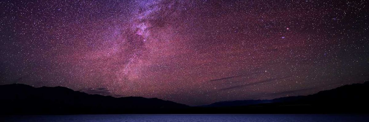 Starry night sky with a vibrant Milky Way over a dark horizon and water.