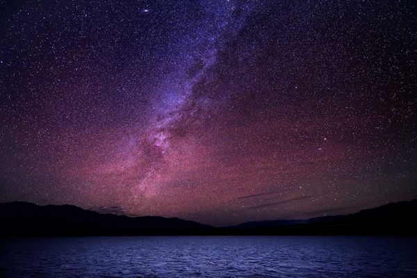 Starry night sky with a vibrant Milky Way over a dark horizon and water.