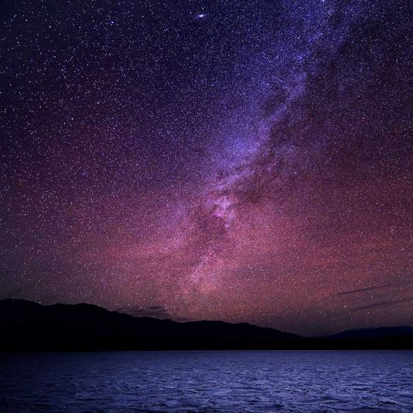 Starry night sky with a vibrant Milky Way over a dark horizon and water.