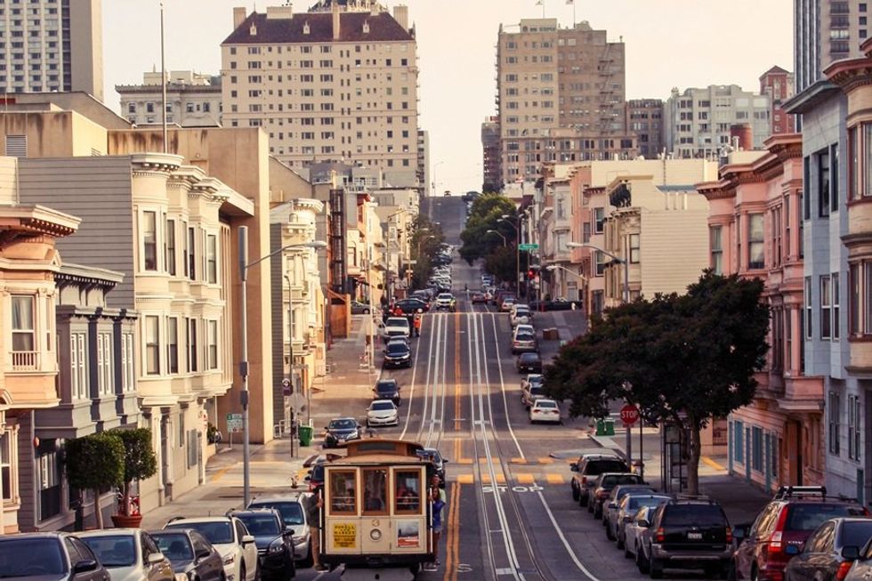 Steep city street with a cable car and lined with parked cars and colorful buildings.