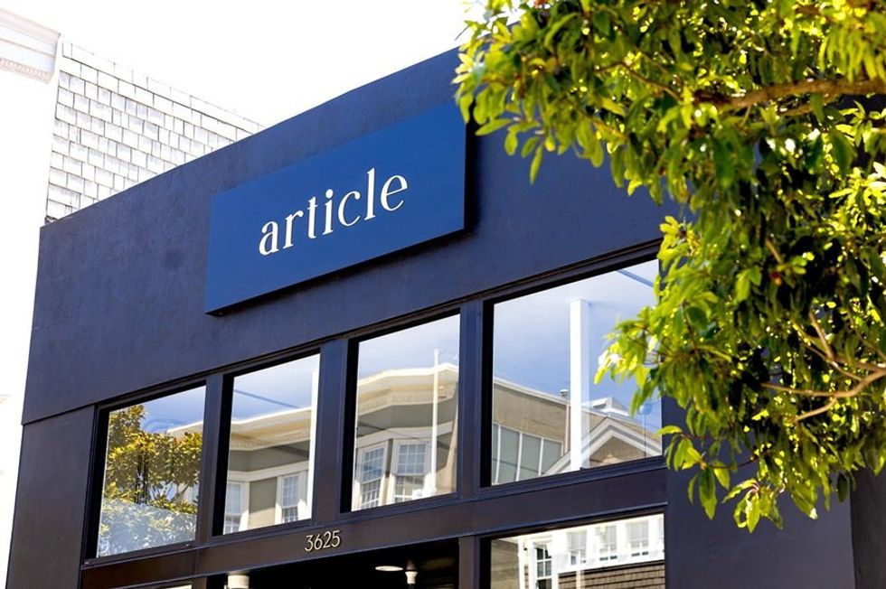 Storefront with "article" sign, large windows, and tree in foreground.